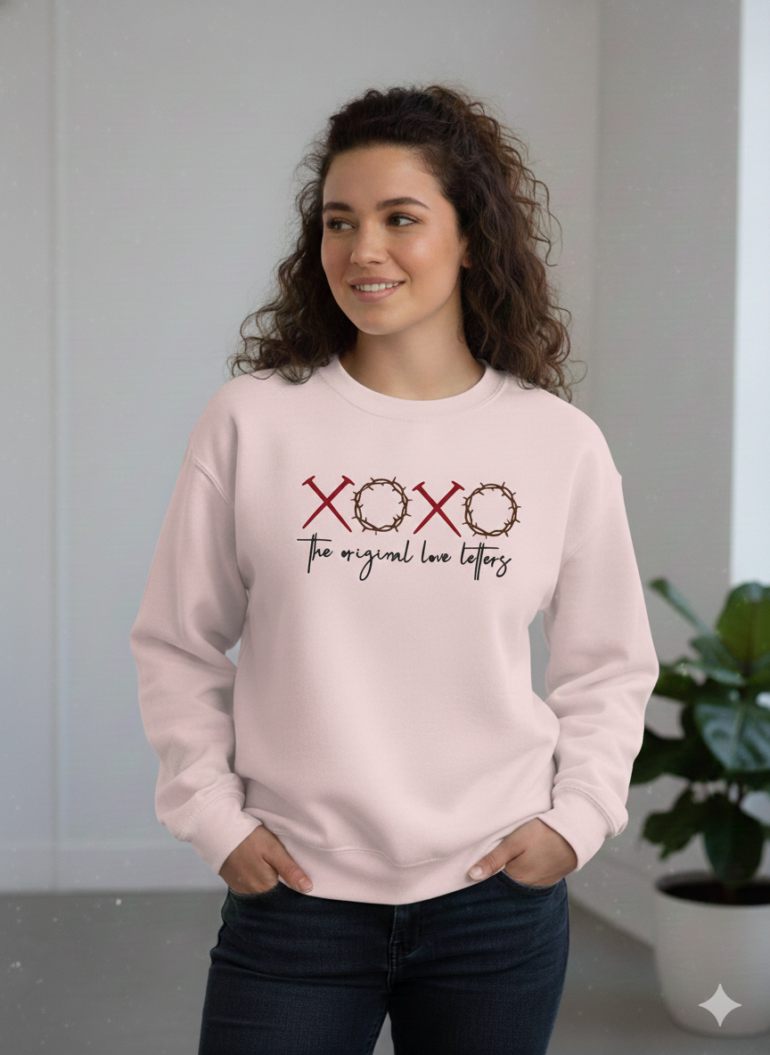 Woman wearing a light pink sweatshirt with 'XOXO The original love letters' text.