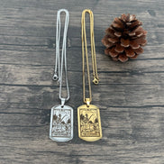 Two necklaces with pendant tags on a wooden surface, one silver and one gold, with a pine cone beside them.