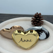 Gold heart-shaped dish with a custom name engraved, surrounded by two other heart-shaped dishes on a white surface.