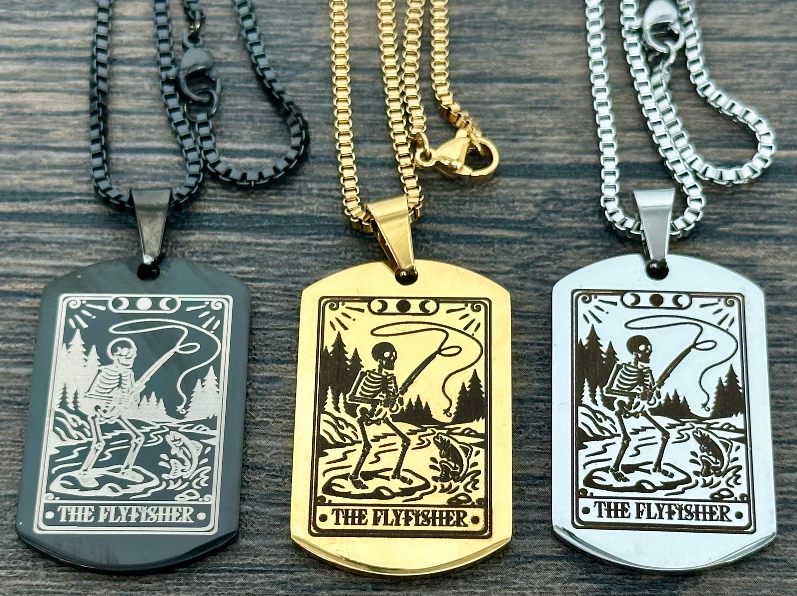 Three dog tag necklaces with 'The Flyfisher' design on a wooden surface.