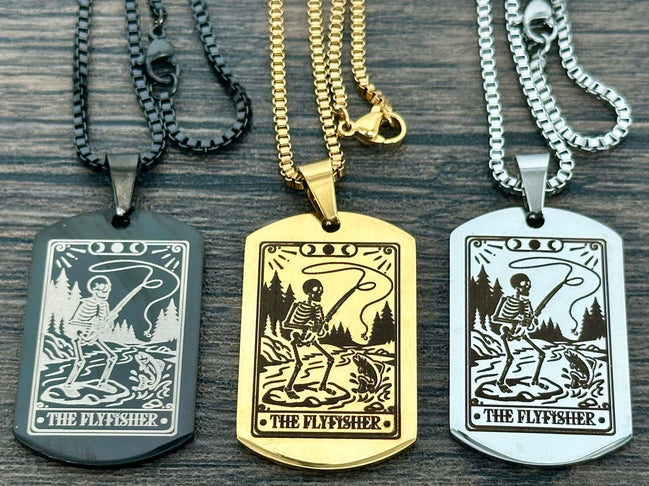 Three dog tag necklaces with 'The Flyfisher' design on a wooden surface.