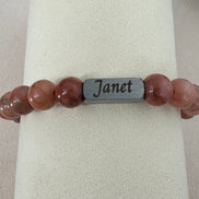 Bracelet with pink beads and a silver tag labeled  with an engraving of a name