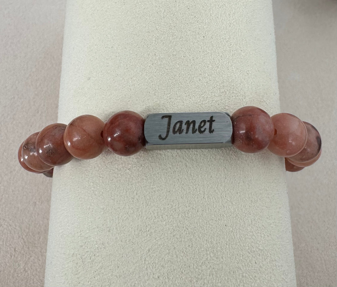 Bracelet with pink beads and a silver tag labeled  with an engraving of a name