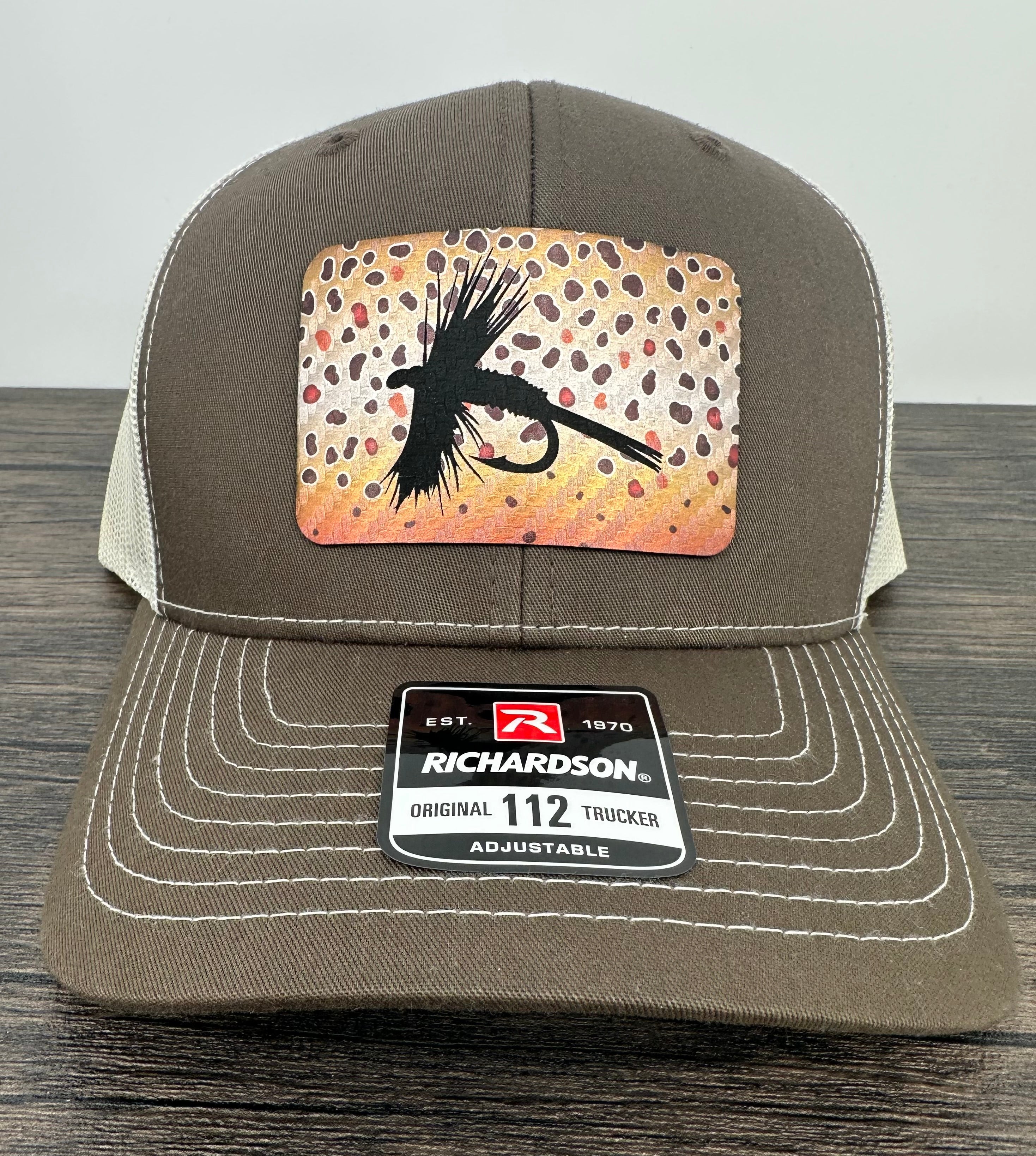 A brown and beige fly fishing hat with a laser engraved fly on a brown trout printed patch