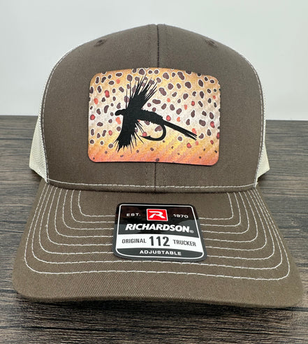 A brown and beige fly fishing hat with a laser engraved fly on a brown trout printed patch
