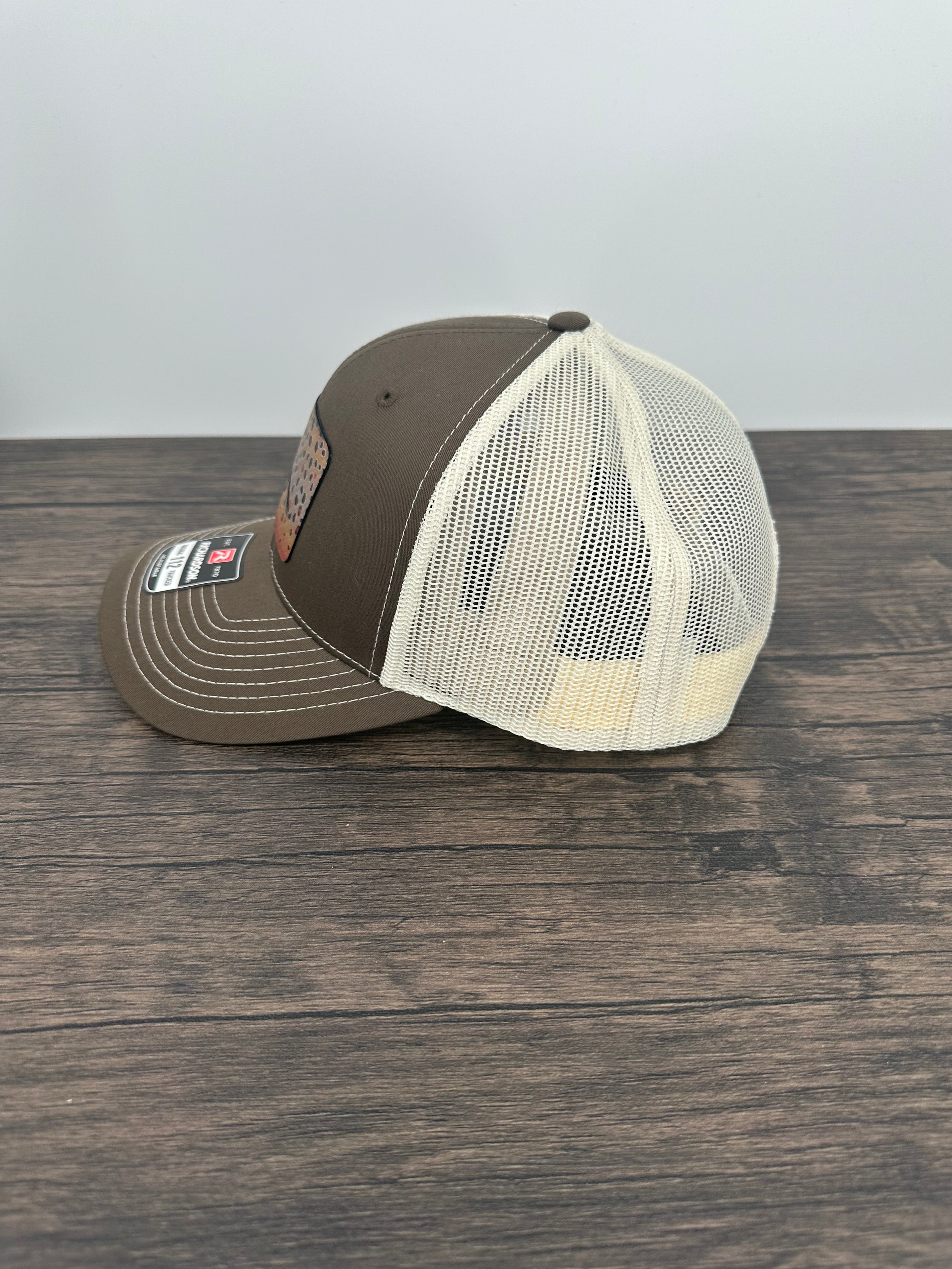 Side view of A brown and beige fly fishing hat with a laser engraved fly on a brown trout printed patch