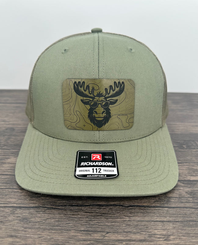 Green cap with a  moose wearing sunglasses  patch