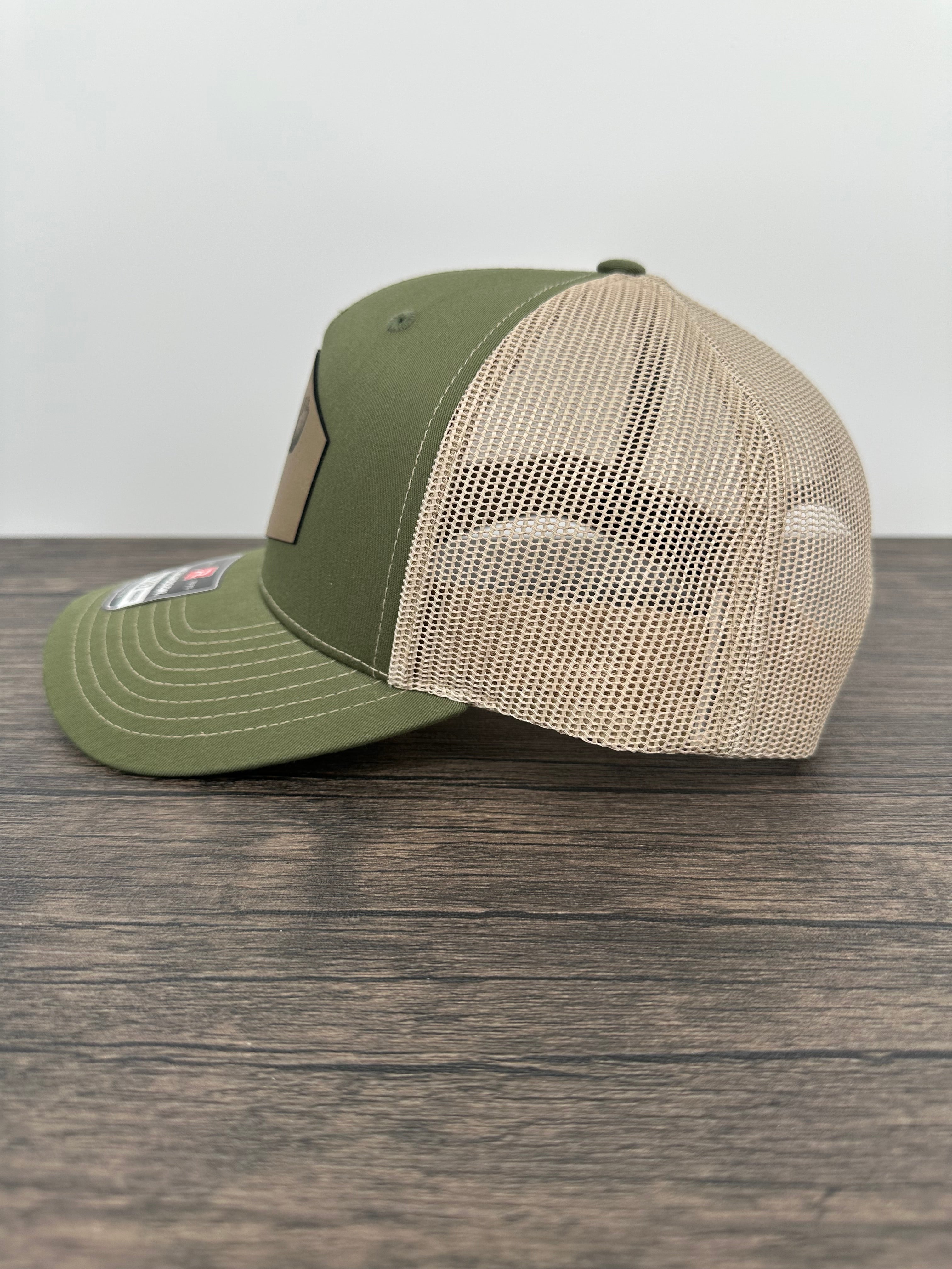 Side view of a Green and beige trucker hat with moose  wearing a beanie and sunglasses that has been laser engraved on a leatherette patch on the front of the hat