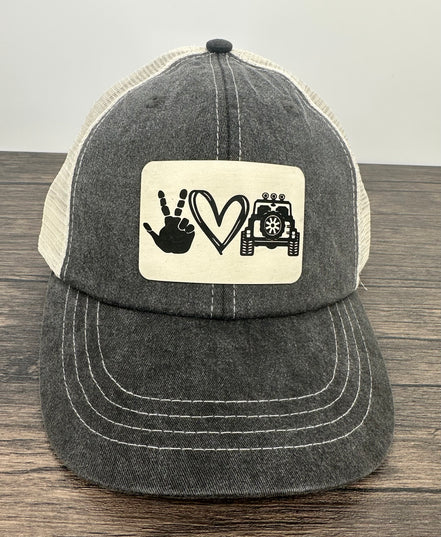 Black and white cap with a patch featuring hand signs, a heart, and a jeep on a wooden surface.