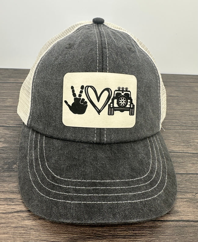 Black and white cap with a patch featuring hand signs, a heart, and a jeep on a wooden surface.