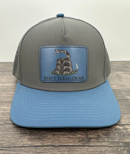 Gray and blue cap with a snake emblem and 'Don't Tread on Me' text on a wooden surface.