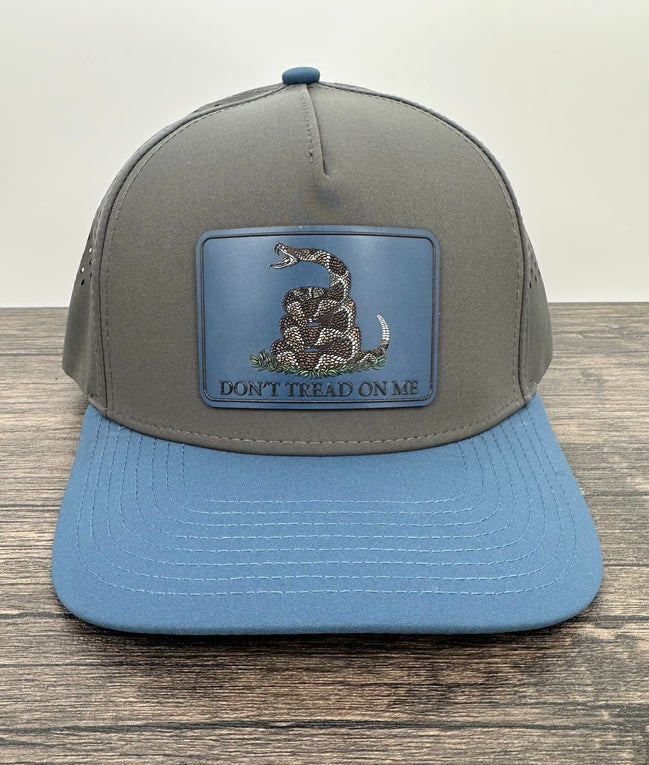 Gray and blue cap with a snake emblem and 'Don't Tread on Me' text on a wooden surface.