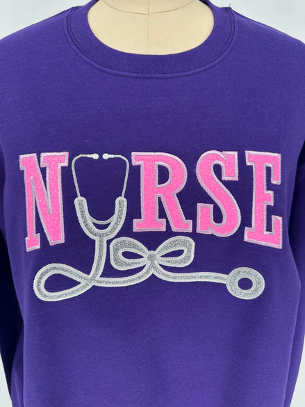 Purple shirt with 'NURSE' and stethoscope graphic in pink and silver on a white background