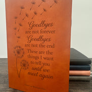 Brown leatherette grief journal book with engraved text and dandelion designs on a wooden surface.