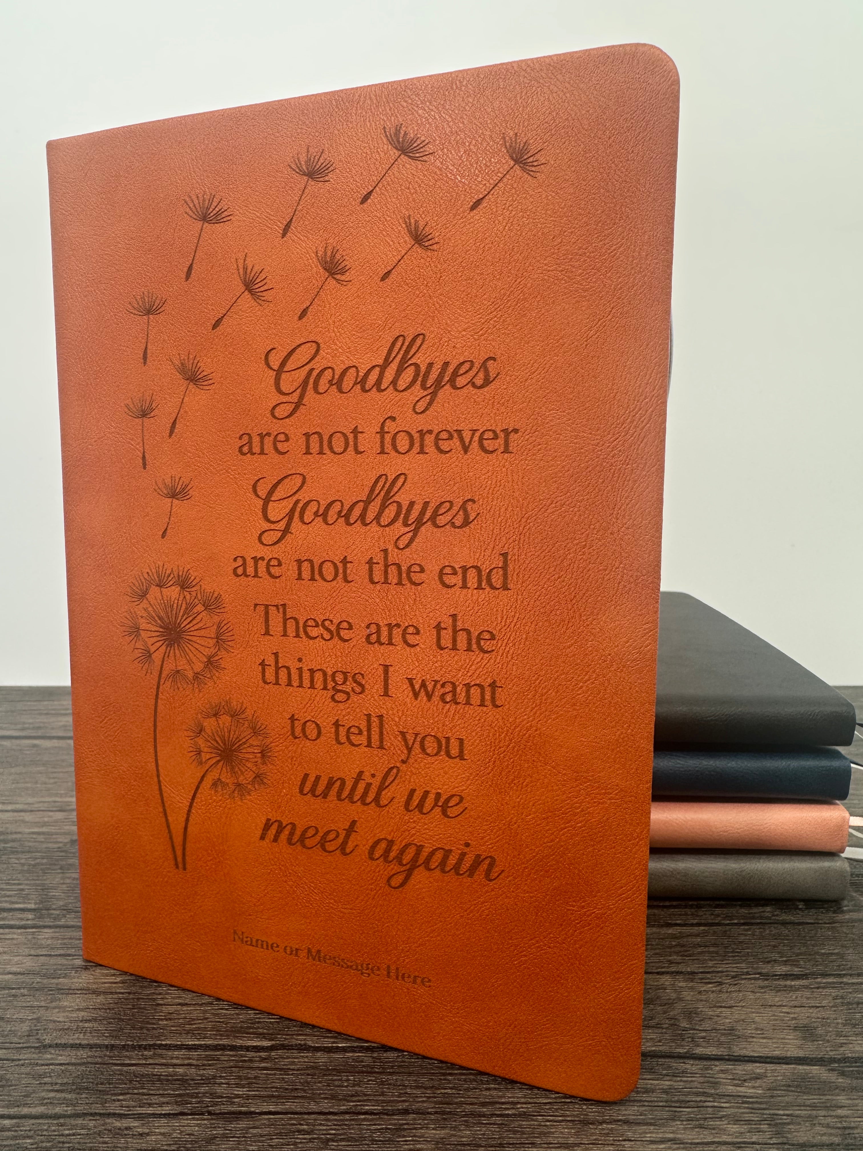 Brown leatherette grief journal book with engraved text and dandelion designs on a wooden surface.