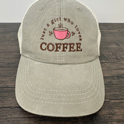 Beige cap with coffee-themed text and pink cup graphic on a wooden surface