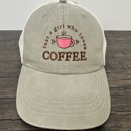 Beige cap with coffee-themed text and pink cup graphic on a wooden surface