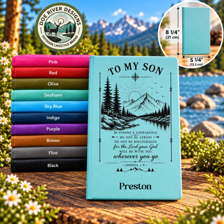 A stack of personalized hardcover journals in various colors is displayed outdoors on a wooden surface with wildflowers and a mountain backdrop. The front journal is light blue with a black graphic of a mountain and pine trees, and the text 'TO MY SON' and 'Preston'.