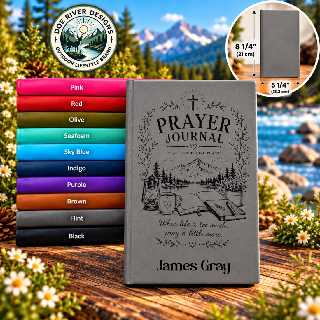 A personalized gray prayer journal standing on a wooden surface with a stack of other journal color options behind it. The main journal shows the engraved text 'PRAYER JOURNAL' and the name 'James Gray.