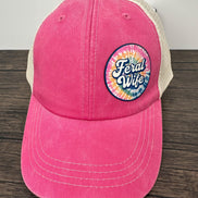 Pink cap with 'Feral Wife' logo on a wooden surface