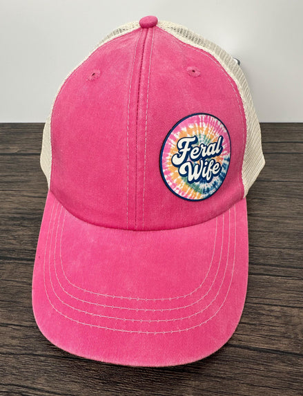 Pink cap with 'Feral Wife' logo on a wooden surface